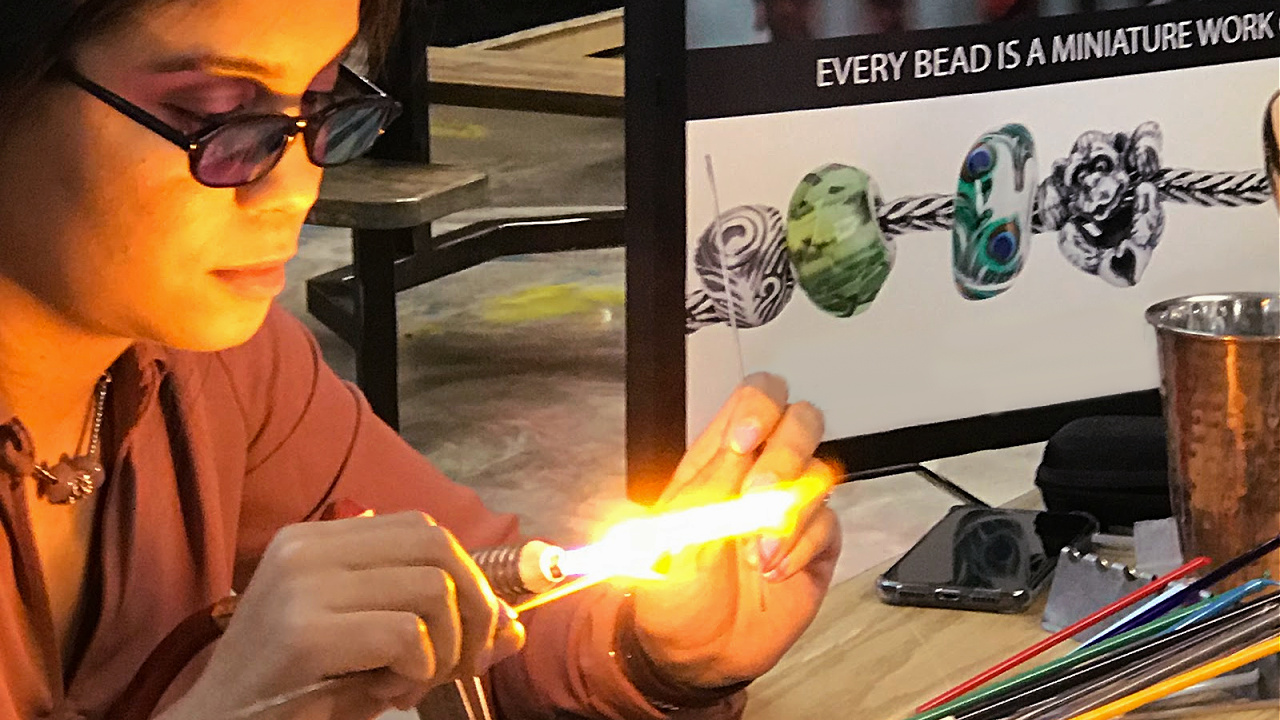 A female melting glass in a hot flame to show how glass beads are made