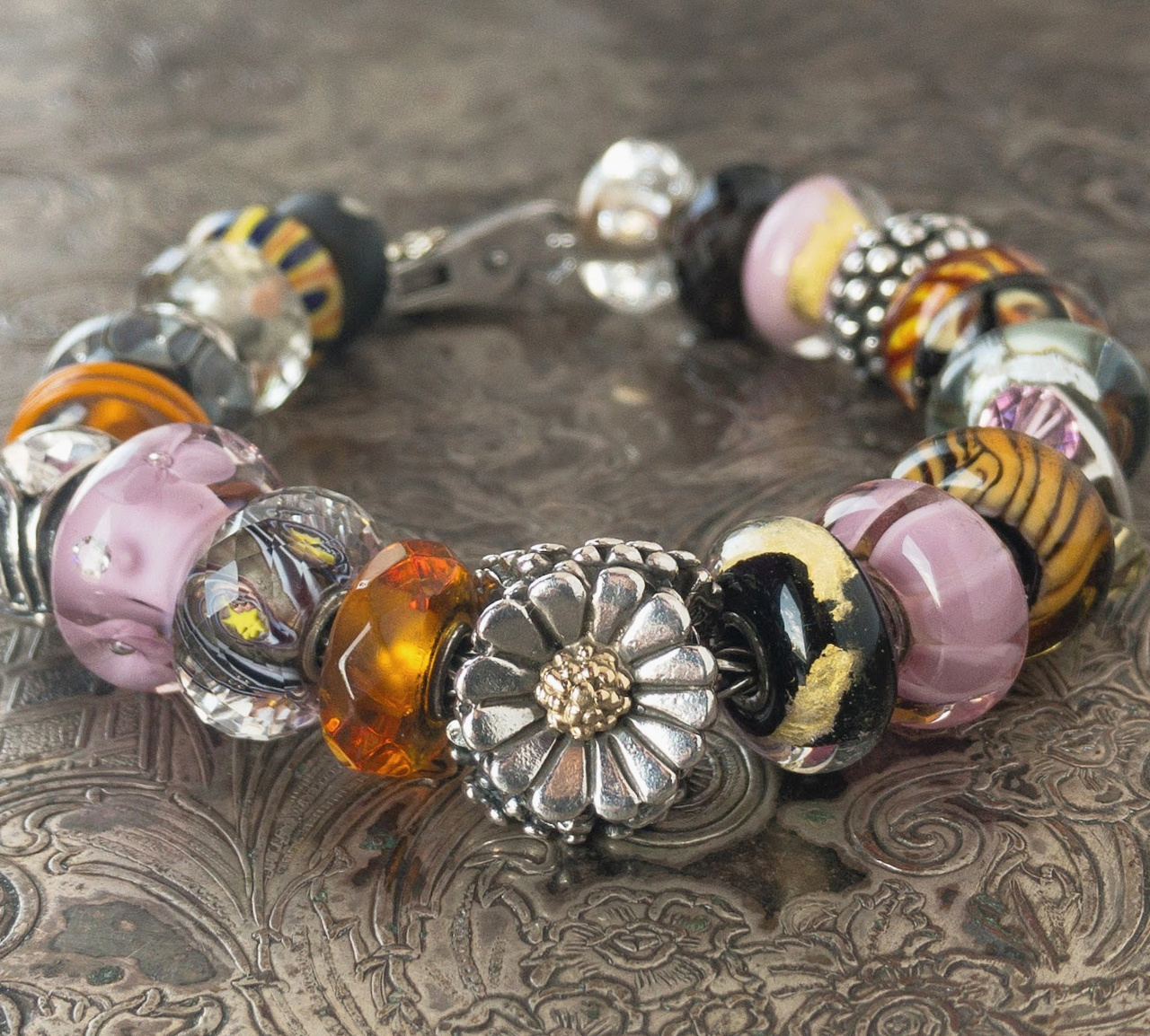A sterling silver bracelet full of pink, black, amber, crystal and sterling silver Trollbeads, featuring a Trollbeads "Daisy" bead. 