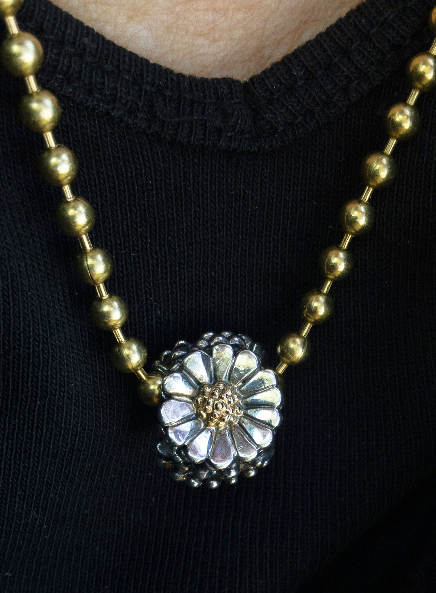 Trollbeads sterling silver and 18 karat gold "Daisy" bead on a gold-toned ball chain, worn as a necklace.