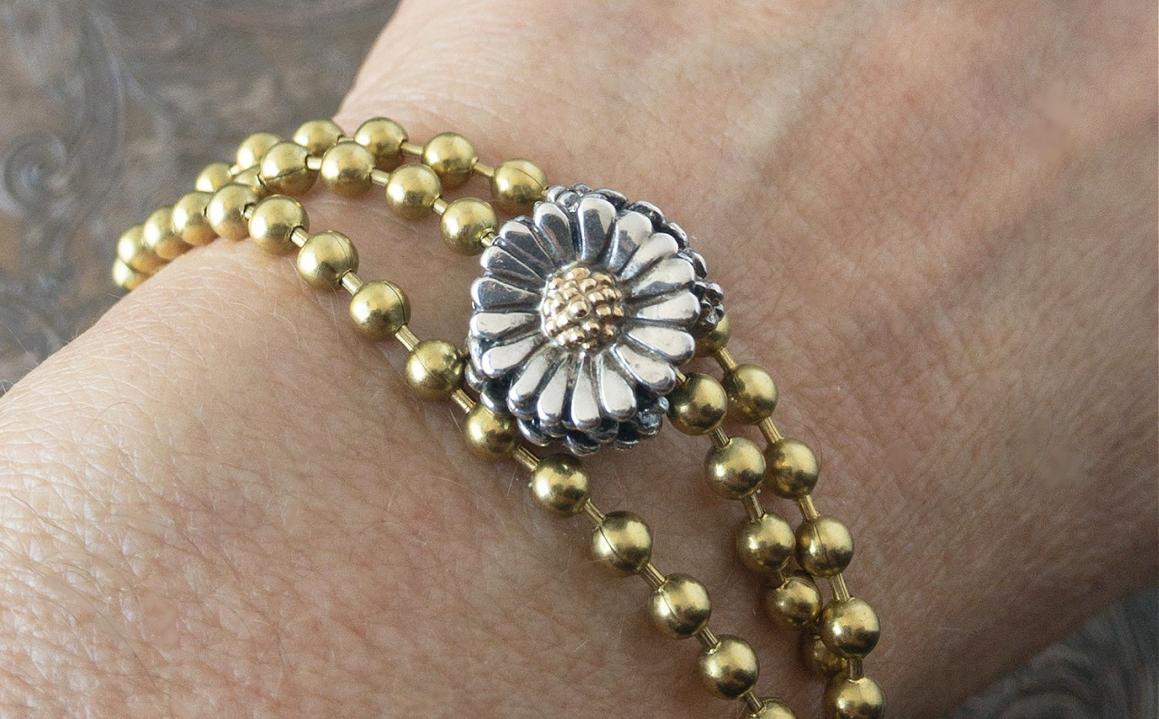 Trollbeads sterling silver and 18 karat gold "Daisy" bead on a gold-toned ball chain, wrapped around a wrist.