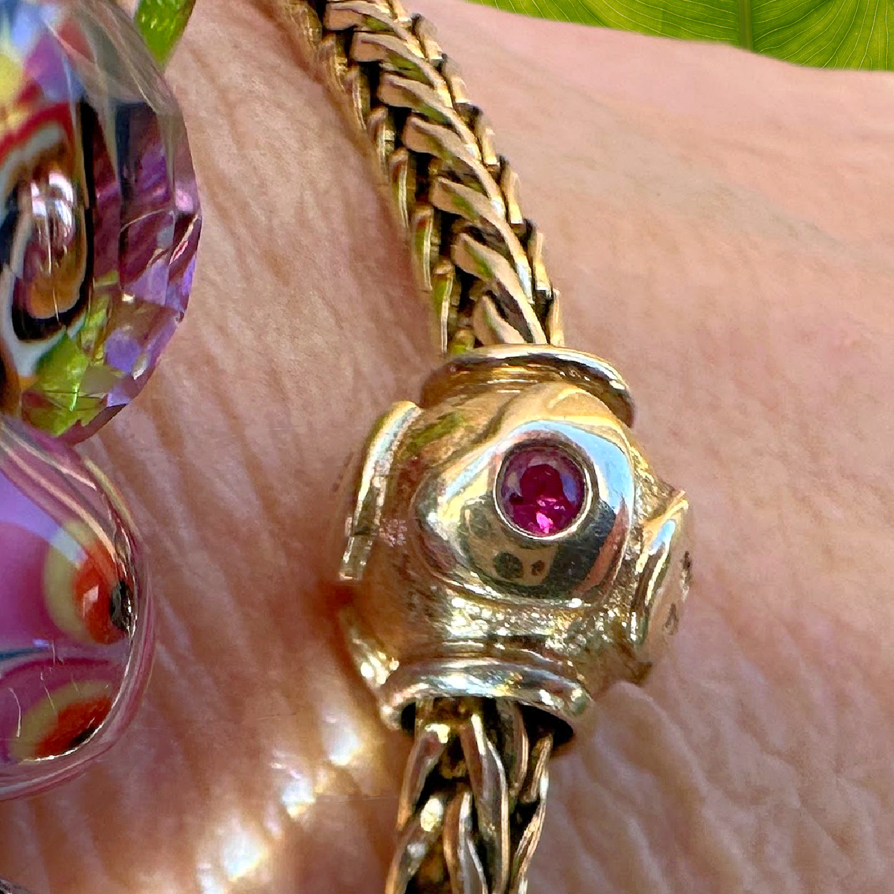 A wrist wearing an 18KT gold bracelet and gold heart bead with a ruby  in the centre.
