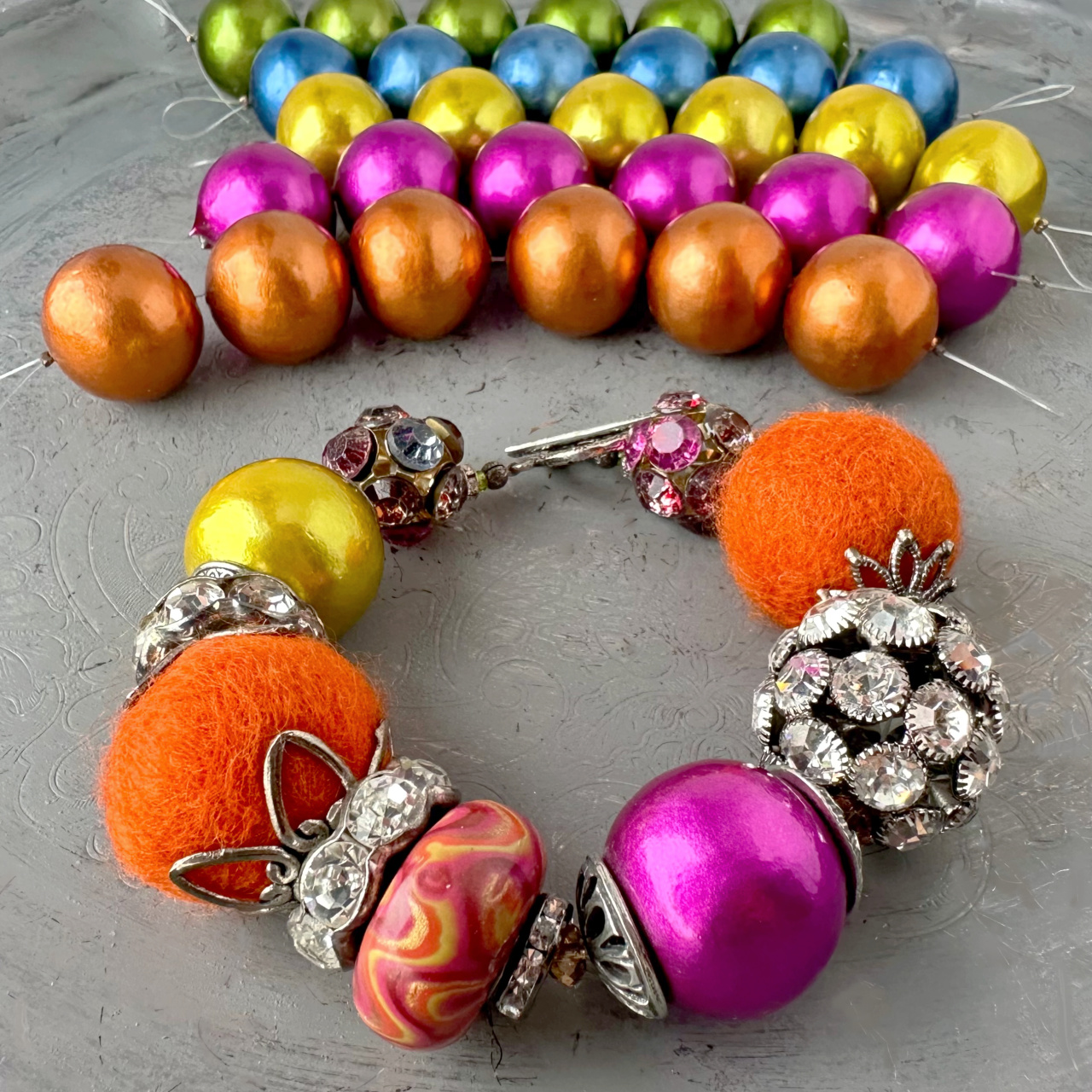 Strands of new Cotton Pearl beads in background, with a chunky, handcrafted bracelet in foreground, featuring two new cotton pearl beads.