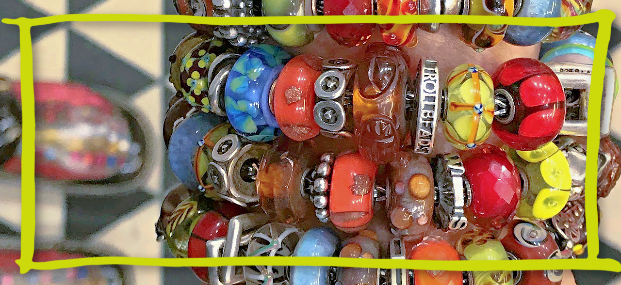 A close-up photo of a stack of colourful Trollbeads bracelets shown on a wrist.